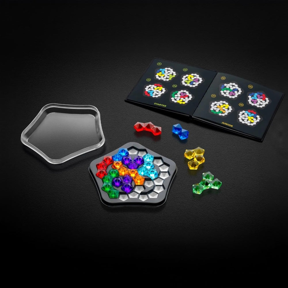 A colourful logic puzzle game set displayed on a dark background, including a clear pentagon lid, a black pentagon tray filled with brightly coloured pieces, loose coloured pieces, and the challenge book