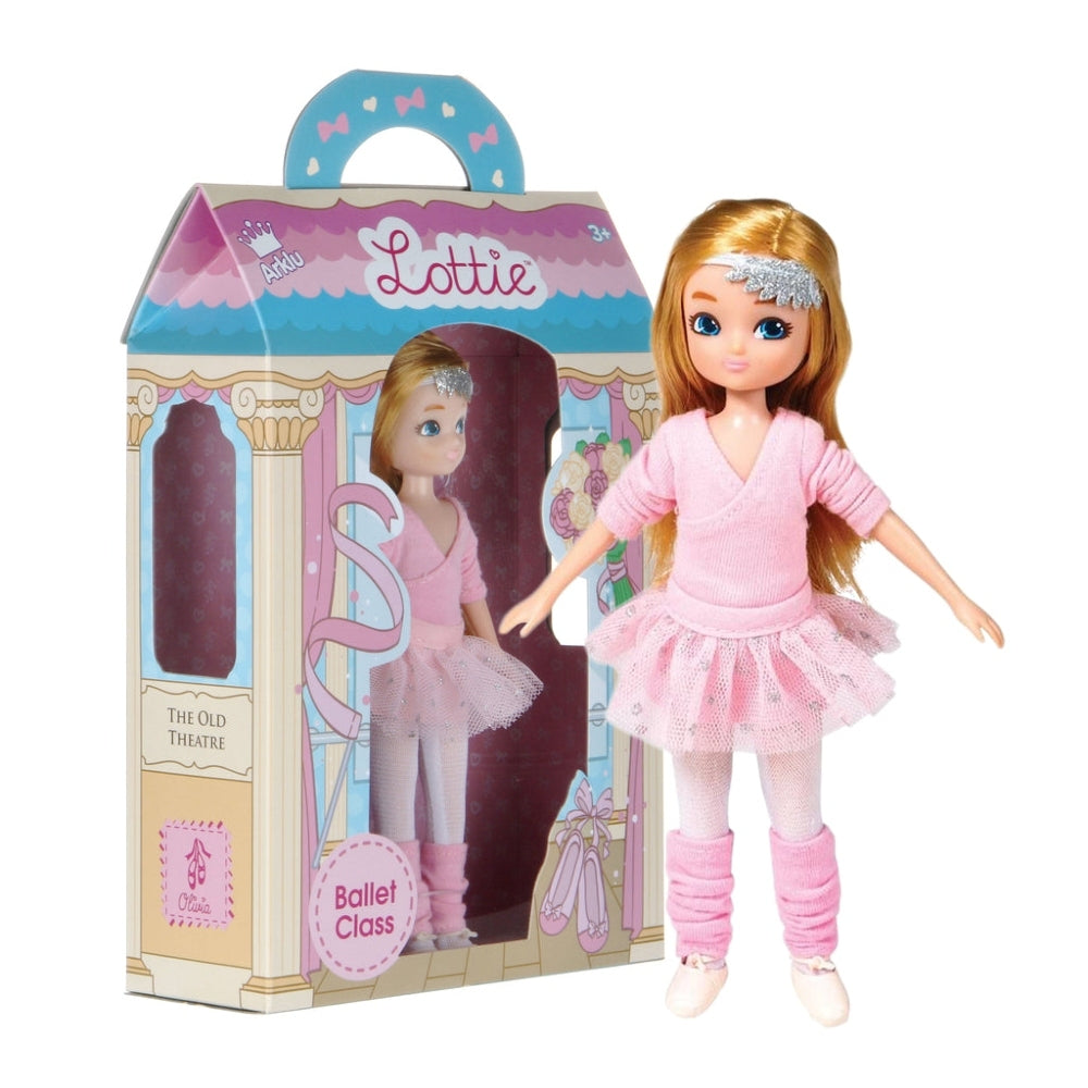 The ballet themed box for the Ballet Class Lottie doll, with a blond haired Lottie doll standing next to it in a pink wrap-around cardigan, pink tutu, pink leg warmers and ballet shoes