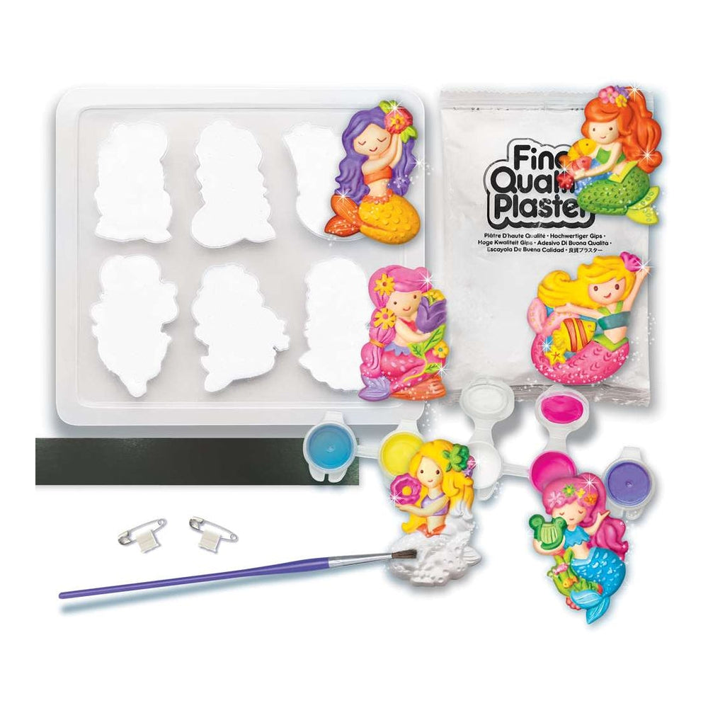 Mermaid-themed plastic plaster painting kit with white plastic moulds, paint pots, a paintbrush, magnetic strip, pins, and a package labelled 'Fine Quality Plaster'.