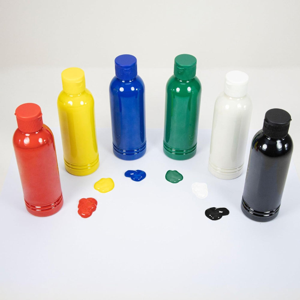 Six plastic paint bottles in red, yellow, blue, green, white, and black, arranged in a row on a white background with small dollops of paint in front of each bottle.