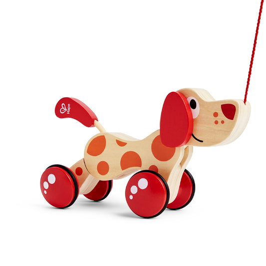 Wooden toy dog for Hape with red wheels and a pull along string on a white background