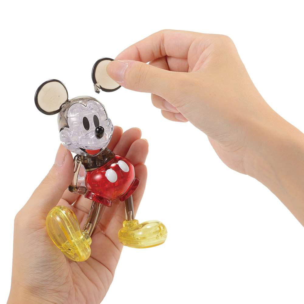 Transparent collectable 3D puzzle Mickey Mouse figurine with coloured accents held by a hand on a white background